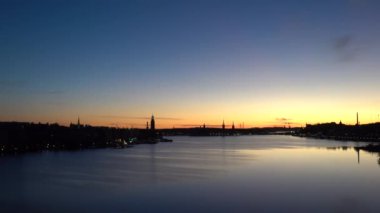 Stockholm, İsveç. Malaren Gölü 'ndeki Riddarfjarden körfezi üzerinde gün doğumu manzarası ve Batı Köprüsü' nden Belediye Binası ve Gamla Stan.. 