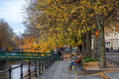 Uppsala, Sweden Oct 28, 2024 Pedestrians on the emabankment of the Uppsala Fyrisan river. clipart