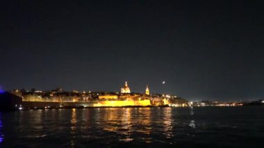 Valletta, Malta. Valletta Limanı 'na gece yaklaşan bir gemi ve tarihi yapı ve Balo' nun kalesi ve antik şehir duvarları aydınlandı..