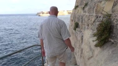 Valletta, Malta Erkek bir turist Akdeniz 'deki kayalıkların altında dar bir patika boyunca yürüyor. 