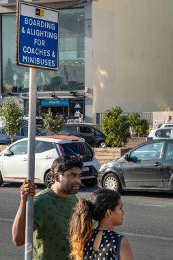 Valletta, Malta 3 Kasım 2024 Sliema bölgesindeki otobüs durağında Asyalı bir erkek ve kadın duruyor..