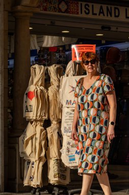 Valletta, Malta Nov 4, 2024 A woman pedestrian walks past a tourist shop selling Malta  emblazoned bags in the sunset on Republic Street. clipart