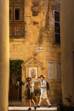 Rabat, Malta, 5 Kasım 2024 Bir adam ve kameralı bir kadın dar bir resim geçidinde yürüyorlar.
