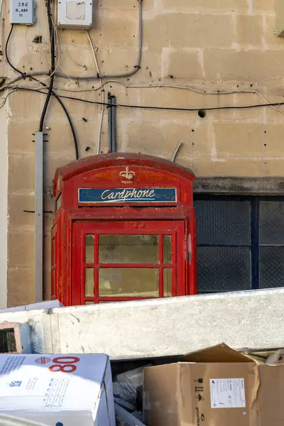 Mdina, Malta, 6 Kasım 2024 Bir yığın karton kutunun arkasına saklanmış eski ve terk edilmiş bir kırmızı telefon kulübesi.