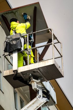 Stockholm, İsveç 20 Kasım 2024 Bir şehir işçisi Liljeholmskajen 'de bir gökdelen üzerinde yağmur örtüsünün altını temizliyor.