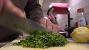 Bir aşçı evcil bir mutfakta maydanozu büyük bir bıçakla doğruyor.
