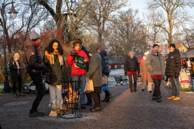 Uppsala, İsveç 7 Aralık 2024 İnsanlar Wik 's Castle' daki bir Noel pazarına katılıyor ve küçük bir ateşin etrafında ısınıyorlar..