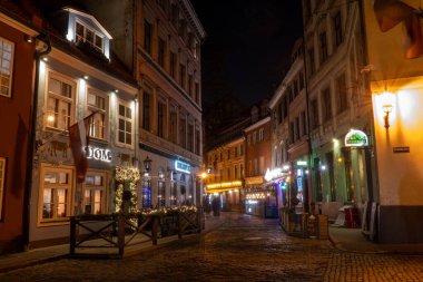 Riga, Letonya 10 Aralık 2024 Restoranlar, dükkanlar ve sokak lambaları Eski Twon 'da eski bir parke taşlı sokakta.