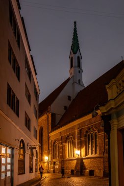 Riga, Letonya 10 Aralık 2024 'te yayalar sabahın erken saatlerinde aydınlatılmış St. John Kilisesi' nin önünden geçtiler.