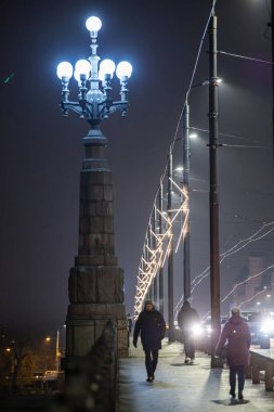 Riga, Latvia Dec 10, 2024 People walking over the Stone Bridge at night. clipart