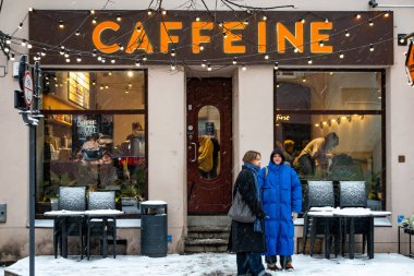 Vilnius, Lithuania Jan 6, 2025 Two women stand outside a coffee shop called Caffeine in the snow. clipart