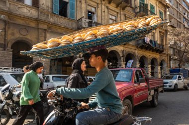 Kahire, Mısır 22 Ocak 2025. Genç bir adam motosikletle taze ekmek getiriyor. Kafasını dengeleyerek..