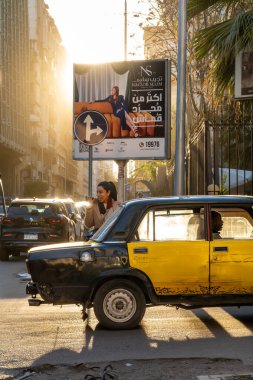 Alexandria, Egypt Jan 27, 2025 A smart dressed woman with a phone crosses the street at sunset  on Gamal Abdel Nasser Street in the downtown. clipart