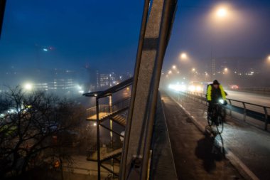 Stockholm, İsveç 27 Şubat 2025 sisli bir sabahta Liljeholmsbron 'da bisiklet yolunda bir bisikletçi veya Liljeholmen Köprüsü.