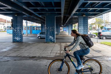 Zagreb, Hırvatistan 24 Mart 2025 Bir genç kadın bir üst geçidin altında bisiklete biniyor. Ve tramvay..