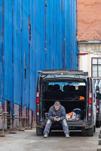 Zagreb, Hırvatistan 24 Mart 2025 Bir işçi minibüsünün arkasında oturuyor ve Ul üzerinden telefonunu kontrol ediyor. Pavla Rittera Vitezovieva.