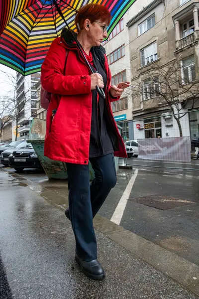 Zagreb, Hırvatistan 24 Mart 2025 Kırmızı ceketli üst düzey bir kadın yağmurda Yukarı Kasaba 'da şemsiyeyle yürüyor.