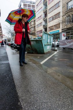 Zagreb, Hırvatistan 24 Mart 2025 Kırmızı ceketli üst düzey bir kadın yağmurda Yukarı Kasaba 'da şemsiyeyle yürüyor.