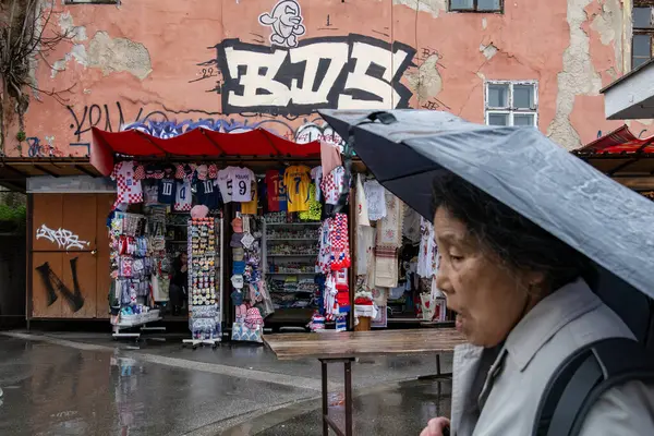 Zagrep, Hırvatistan 24 Mart 2025 Asyalı bir turist kadın elinde şemsiyeyle Upper Town 'da bir turist dükkanının önünden geçiyor ve duvar yazısıyla ev cephesinde yürüyor.