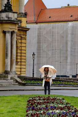 Zagreb, Hırvatistan 24 Mart 2025 'te Hırvat Ulusal Tiyatrosu' nun yanındaki parkta yağmurda şemsiyeli bir kadın ayakta duruyor.