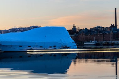 Stockholm, İsveç 2 Nisan 2025. Kungsholmen adasında plastikle kaplı bir tekne ve aydınlık bir rıhtım manzarası..