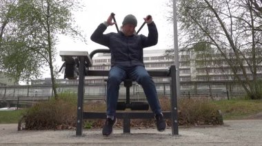 Stockholm, İsveç. Sokak kıyafetleri içinde bir adam parktaki açık hava spor salonunda çalışıyor.. 