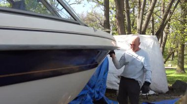 Stockholm, İsveç Teknesi 'nin fiberglas gövdesini balmumuyla cilalıyor. Bir tekne kulübünde tekne sezonu başlamadan önce..  