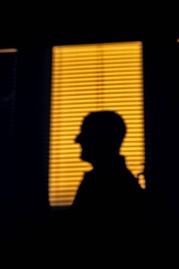 Stockholm, İsveç 'te bir adam güneşli bir pencerenin perdeli yansımasına karşı siluet içinde duruyor..