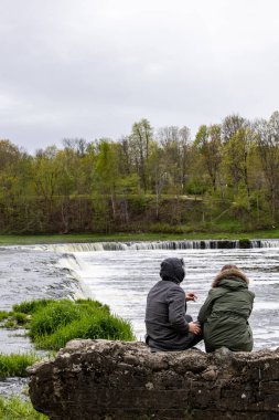 Kuldiga, Letonya 6 Mayıs 2025 Kuldiga şelalesinin yanında oturan bir erkek ve bir kadın veya Venta Rapids, Avrupa 'nın 249 metre çapındaki en geniş şelalesi..
