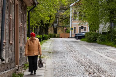 Kuldiga, Letonya 6 Mayıs 2025 Kırmızı şapkalı yaşlı bir kadın kaldırım taşlı bir sokakta yürüyor..