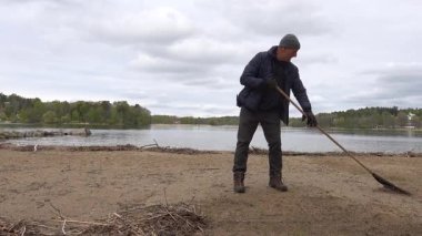Stockholm, İsveç 'te bir adam kışın dökülen dallardan ve yabani otlardan sahil temizler.. 