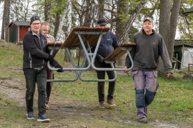Stockholm, İsveç 10 Mayıs 2025 Erkekler bir tekne kulübünün üyelerine ait küçük ormanlık bir adada bir park masası taşıyorlar..