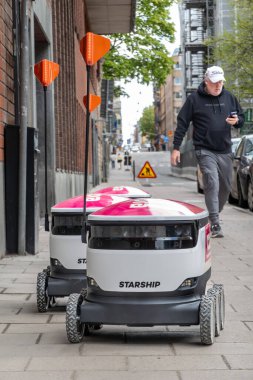 Stockholm, İsveç 11 Mayıs 2025 kaldırımda yemek dağıtım robotlarının yanından geçen yayalar.
