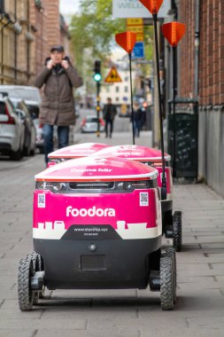 Stockholm, İsveç 11 Mayıs 2025 kaldırımda yemek dağıtım robotlarının yanından geçen yayalar.