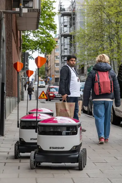 Stockholm, İsveç 11 Mayıs 2025 kaldırımda yemek dağıtım robotlarının yanından geçen yayalar.