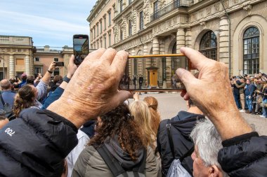 Stockholm, İsveç 18 Mayıs 2025. Turistler Kraliyet Sarayı 'ndaki nöbetçi değişiminin fotoğrafını çekmek için akıllı telefonlarını kullanıyorlar..