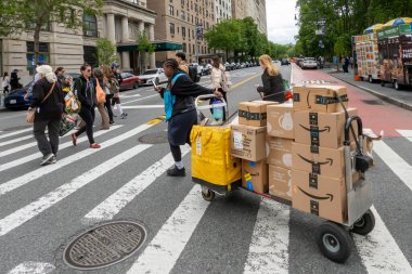 New York, New York, ABD 24 Mayıs 2025 Bir Amazon Prime sürücüsü caddenin karşısındaki kavşakta Amazon Prime paketleriyle bir yük arabası çekiyor..