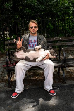 New York, New York, ABD 24 Mayıs 2025 Columbus Bulvarı Açık Sokaklar Festivali 'nde bir adam kucağında yayılmış bir boksör köpeği ile bankta oturuyor..