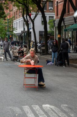 New York, New York, ABD 24 Mayıs 2025 Columbus Caddesi Açık Sokak Festivali 'nin ortasında bir kadın tek başına yemek yiyor..