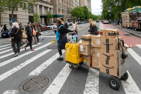 New York, New York, ABD 24 Mayıs 2025 Bir Amazon Prime sürücüsü caddenin karşısındaki kavşakta Amazon Prime paketleriyle bir yük arabası çekiyor..