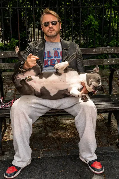 New York, New York, ABD 24 Mayıs 2025 Columbus Bulvarı Açık Sokaklar Festivali 'nde bir adam kucağında yayılmış bir boksör köpeği ile bankta oturuyor..