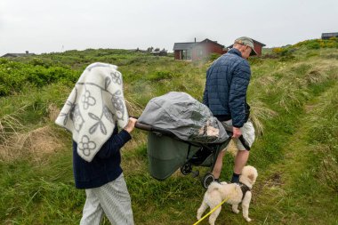 Hirtshals, Danimarka Bir çift yağmur altında kum tepeleri ve yüksek otlar arasında bir bebek arabası taşıyor.