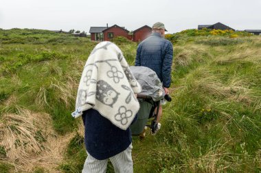 Hirtshals, Danimarka Bir çift yağmur altında kum tepeleri ve yüksek otlar arasında bir bebek arabası taşıyor.