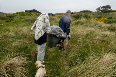 Hirtshals, Danimarka Bir çift yağmur altında kum tepeleri ve yüksek otlar arasında bir bebek arabası taşıyor.