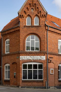 Nykobing Mors, Danimarka 8 Haziran 2025 Şehir merkezinde eski bir kırmızı tuğla bina ve Nykobing yazan bir tabela.
