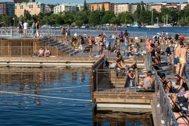 Stockholm, İsveç 19 Temmuz 2025 Arstaviken 'de halka açık ahşap bir açık yüzme platformu olan Marieviksbadet' de güneşlenen kalabalık.