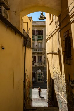 Cagliari, Sardinya, İtalya 6 Ağustos 2025 Pedestrianlar, Via Giuseppe Manno 'da analog bir saatle dar bir geçitten geçtiler..