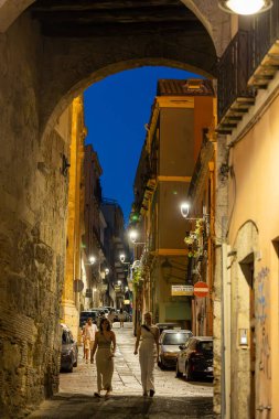 Cagliari, Sardunya, İtalya 8 Ağustos 2025 Kadınlar tarihi şehir merkezinde eski kemerli bir geçitte yürüyorlar.