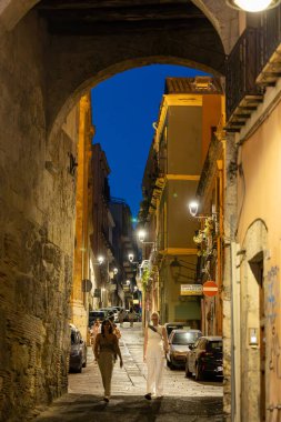 Cagliari, Sardunya, İtalya 8 Ağustos 2025 Kadınlar tarihi şehir merkezinde eski kemerli bir geçitte yürüyorlar.