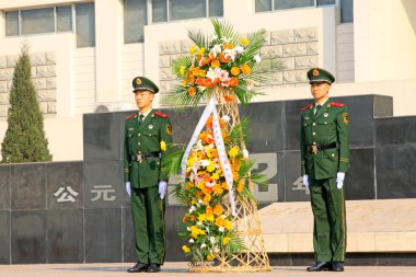 LUANNAN COUNTY - 22 Mart 2014 'te Pan Dai köyü katliam anıtı dış binasında çiçek sepeti taşıyan silahlı polis askerleri, Luannan County, Hebei, Chin